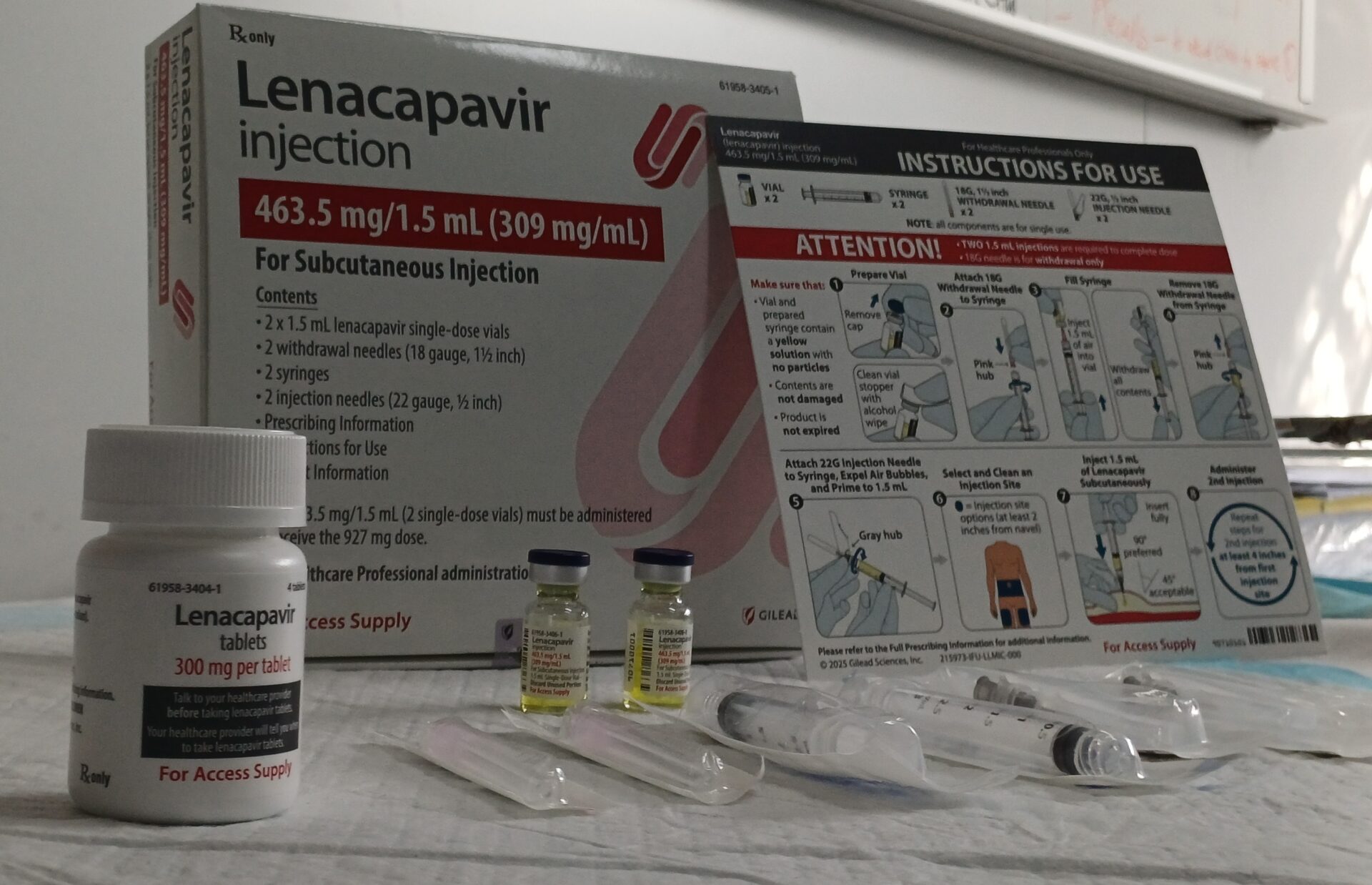 A shot of the contents of the lenacapavir injection kit, showing the box and instruction pamphlet, two vials of the drug, two syringes, and two different sets of needles, with a plastic pill container of the lenacapavir pill.