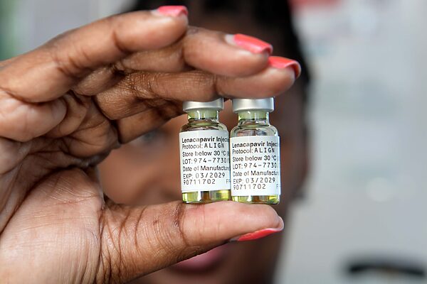 A close-up of a hand, with red, painted fingernails, holding two vials of the lenacapavir injection.