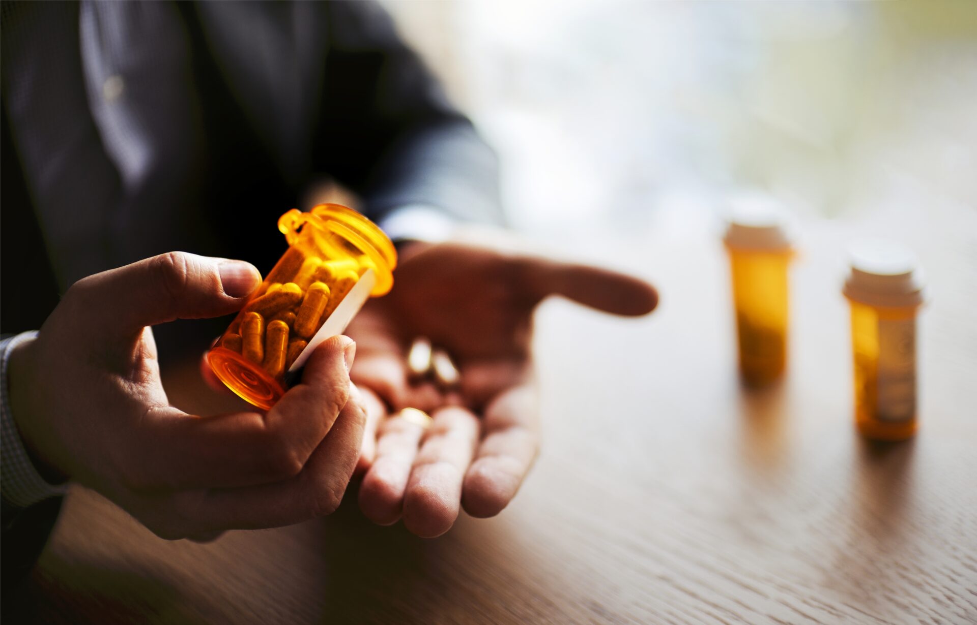 A person holding an orange pill bottle, measuring out two tablets into a their hand